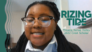 Mikaela Renae Holley smiling while on a virtual phone call. Next to her, green text reads "Rizing Tide, Mikaela Renae Holley, 2022 Crest Scholar."