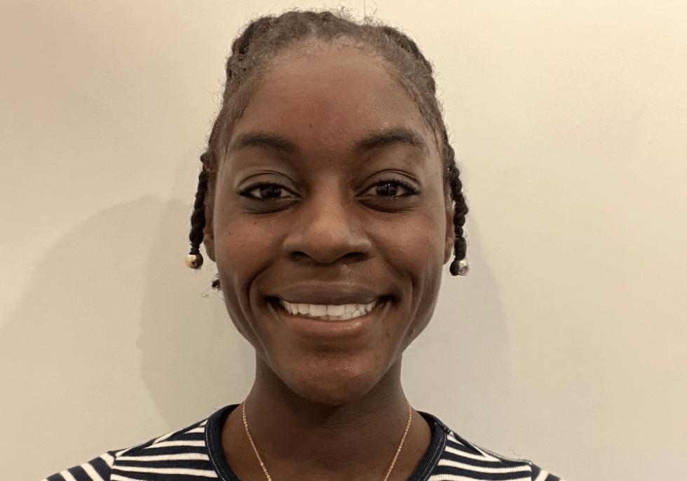 Surge Scholar Dr. Bridget Ochuko smiles for a headshot in front of a plain, beige wall. Her hair is pulled back and she's wearing a black and white-striped shirt.