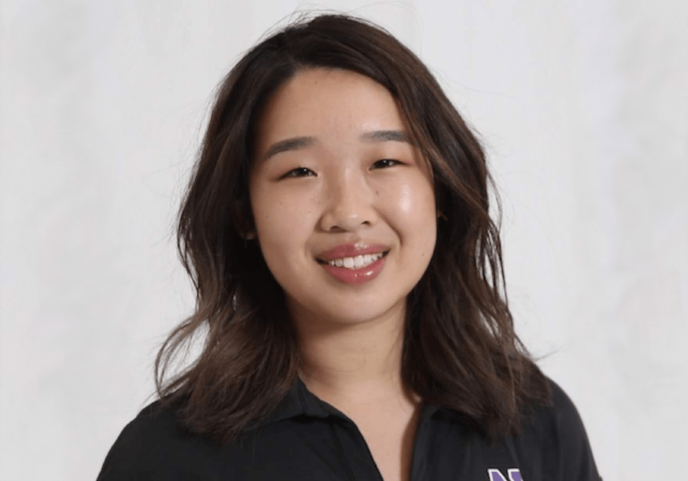 Crest Scholar Jackie Hua smiles for a professional headshot in front of a plain, white background. She's wearing a black polo that has the purple logo of Northwestern University.