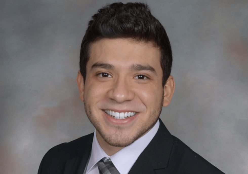 Crest Scholar Said Mendez smiles for a professional headshot against a grey and brown background. He's wearing a suit and tie.